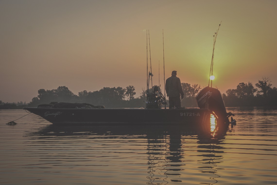 Sven Dombach ein Angler steht auf seinem Mext Wallerboot bei Sonnenuntergang